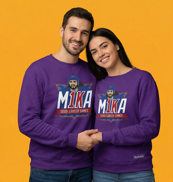"A man and a woman posing together, both wearing matching purple sweatshirts featuring the Mika Zibanejad 'M1KA' 1000 games celebration design, set against a bright yellowish-orange studio background."